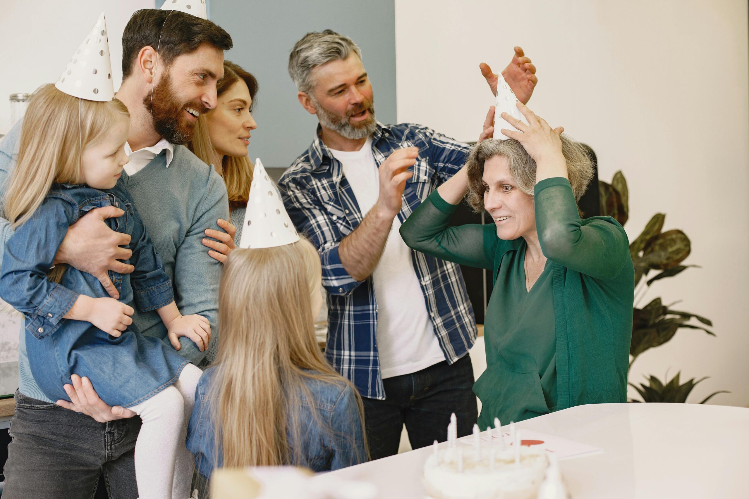 A joyful family birthday celebration with grandparents and children wearing party hats inside a cozy home.